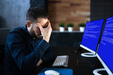 A business person looking at two screens displaying the Blue Screen of Death.