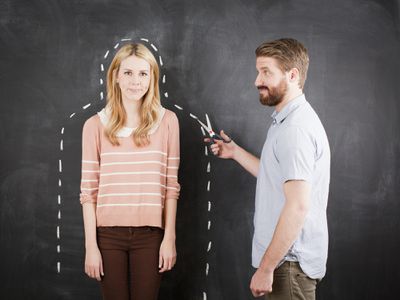 A man pretending to cut along an dotted line drawn around a woman