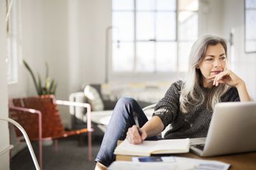 An author looking at a computer screen and writing in a notebook