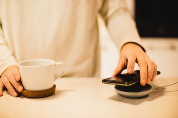 A close up of a table with a wireless charger and a phone placed on it by a person