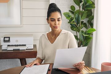 Person reading a freshly-printed paper in front of an HP printer. They look kind pleased about somethingâfor now.