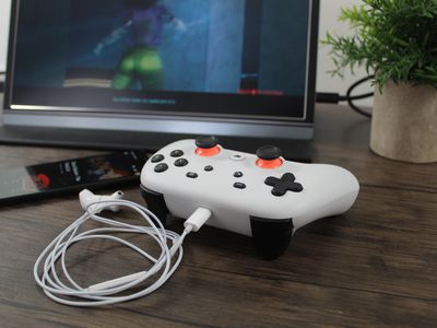 A Stadia controller with a earbud headset plugged in and Cyberpunk 2077 in the background.